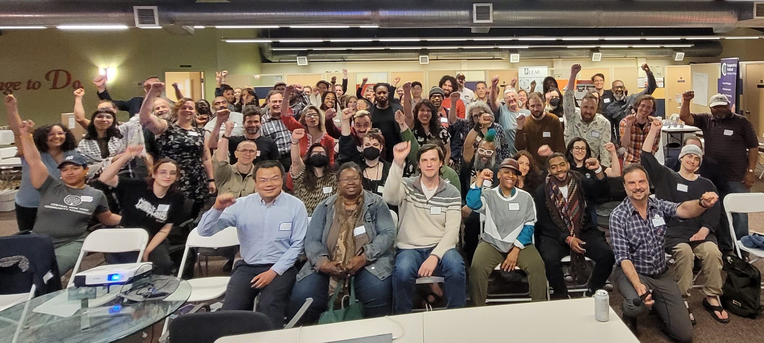 Conference room of attendees cheering and raising their firsts, celebrating the closing of the 2024 NY Cooperative Summit in Syracuse, NY.